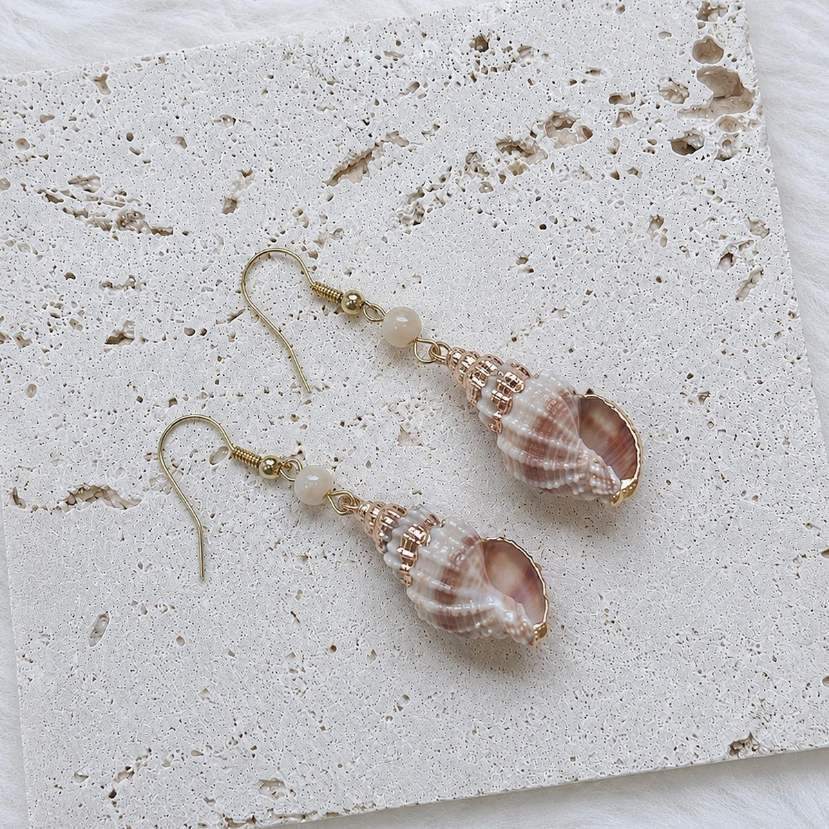 Close view of rounded striped shell earrings with pale beads.
