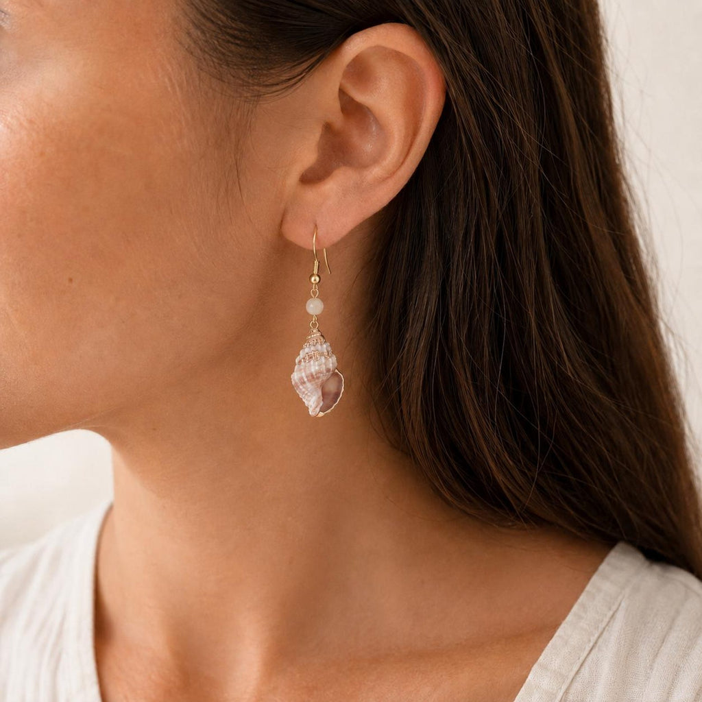 Natural conch-shell drop earring shown worn above an ivory blouse.