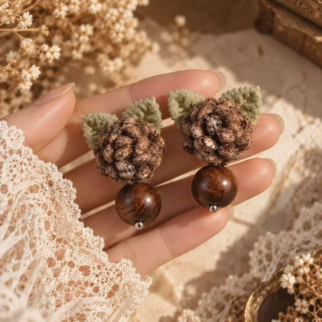 Pair of Hazelwood brown crochet-flower earrings with green leaves and bead drops held in a hand.