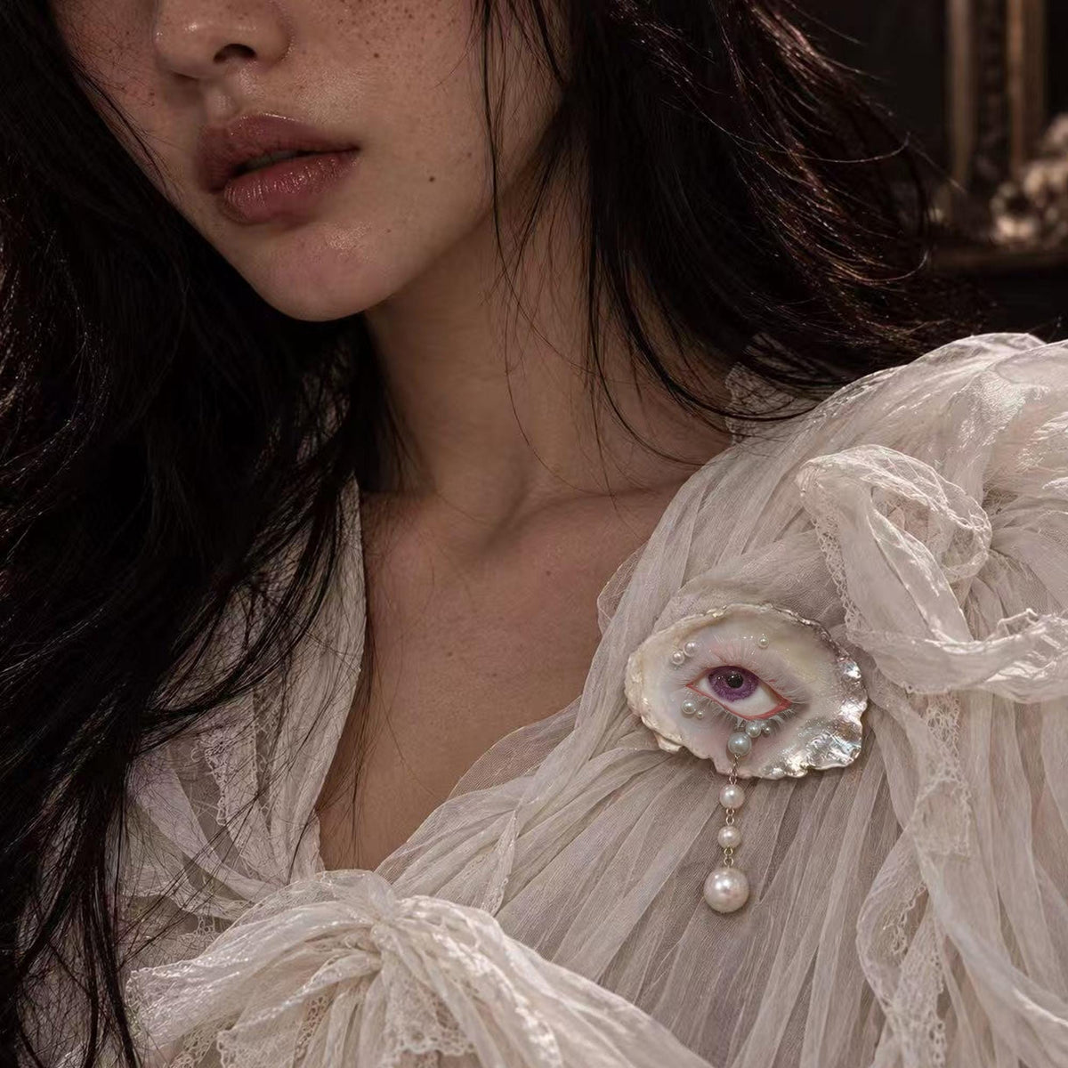 Nyra Lavender Gaze oyster-eye brooch pinned to a pale lace sleeve.