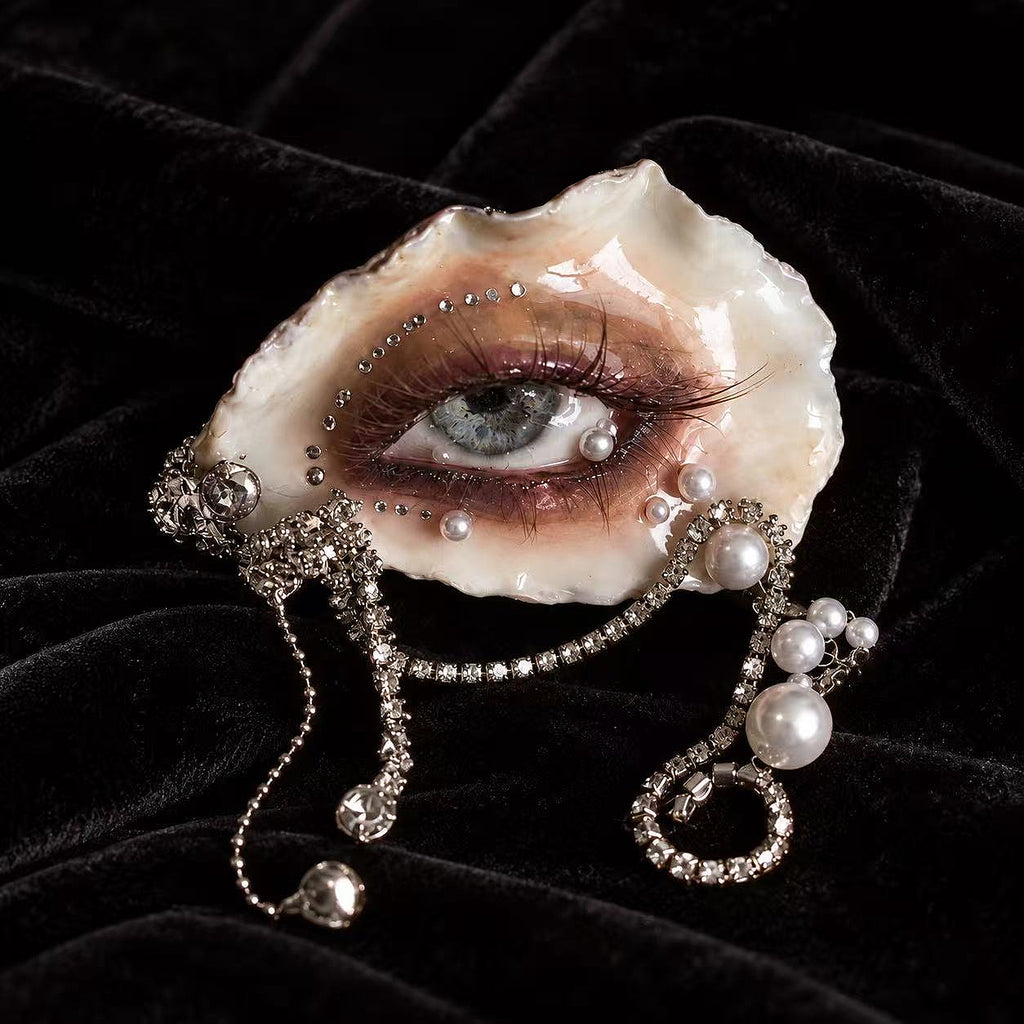 Sereine Eye LV027 — oyster-eye wearable art with smoky bronze makeup, a grey-blue gaze and pearl chain drapes
