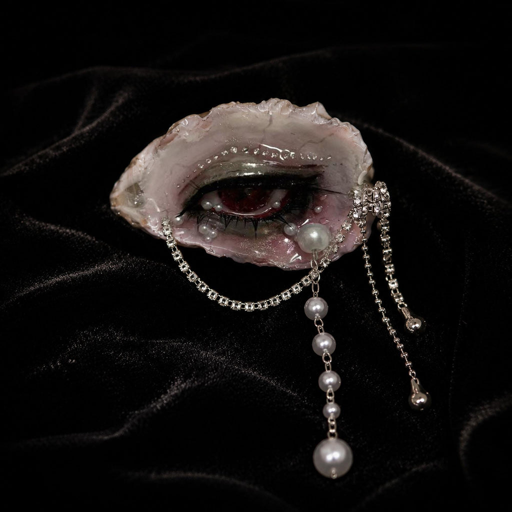 Lilith Veil oyster eye on black velvet showing red pupil, pearls, and silver chains